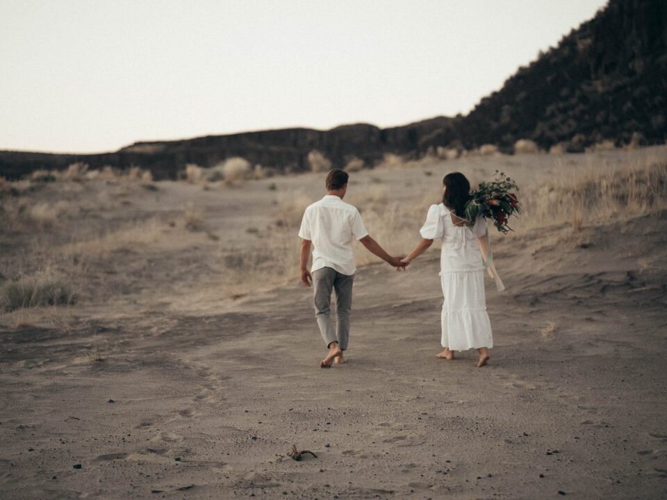 unrecognizable wedding barefoot couple walking on sandy terrain